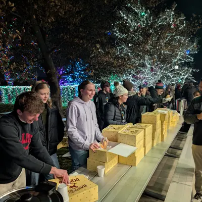 Youth chatting under a park pavilion while handing out donuts with christmas lights lighting the trees in the background